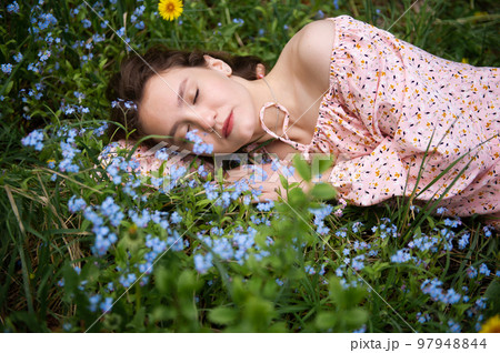 a young girl lies in the green grass with her eyes closed in a pink dress 97948844