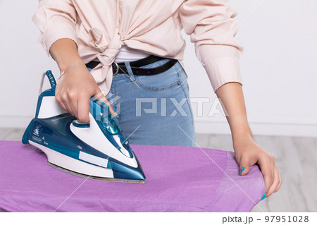 A woman's hand holds an iron and irons a man's shirt on the ironing board. A woman's hand holds an iron and irons a man's shirt on the ironing board. 97951028