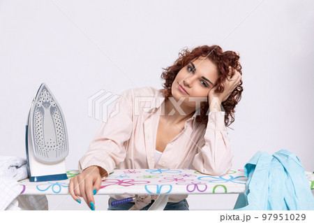 The girl leans her elbow against the ironing board and her hand against her head. The girl leans her elbow against the ironing board and her hand against her head. 97951029