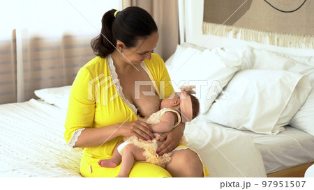 Young woman sitting on the bed and feeding her baby with breast Young woman sitting on the bed and feeding her baby with breast 97951507
