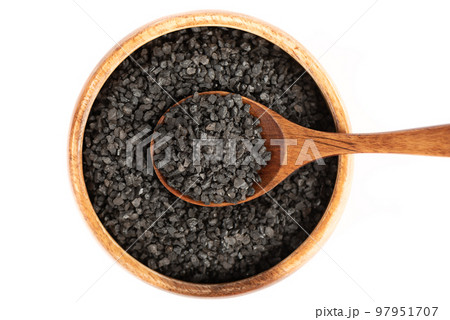 Top view of a bowl with a wooden spoon and black salt on a white background. 97951707