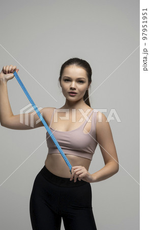 Happy slim brunette woman in sport wear with measuring tape on white background. Positive weight loss diet results. Healthy lifestyles concept. Happy slim brunette woman in sport wear with measuring tape on white background. Positive weight loss diet results. Healthy lifestyles concept. 97951951