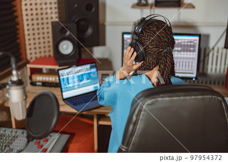 Rear view of a radio presenter, anchor woman, sound engineer wearing headphones and working in broadcasting studio Rear view of a radio presenter, anchor woman, sound engineer wearing headphones and working in broadcasting studio 97954372