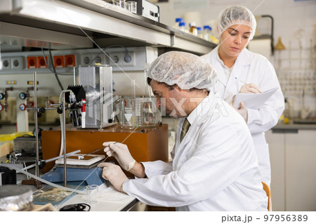 Latin male scientist using microscope while female chemist taking notes in lab Latin male scientist using microscope while female chemist taking notes in lab 97956389