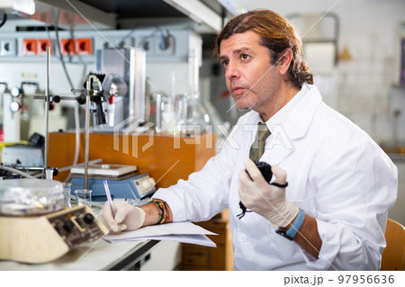 Male scientist engaged in research in chemical laboratory, noting results in chart 97956636