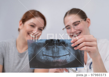 A woman doctor and a patient at the reception are discussing an x-ray of the jaw. 97960373