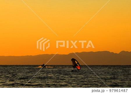 冬の逗子海岸の夕暮れ、オレンジ色に染まる空と海でウィンドサーフィンを楽しむ若者 冬の逗子海岸の夕暮れ、オレンジ色に染まる空と海でウィンドサーフィンを楽しむ若者 97961487