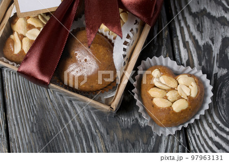 Homemade caramel. Brown caramel candies. Creamy sweets with peanuts. On pine boards. Some of them are packed in a box and tied with a ribbon. 97963131
