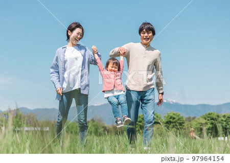 空の見える公園で手を繋いでジャンプして遊ぶ子供と両親のアジア人家族・ファミリーイメージ 97964154
