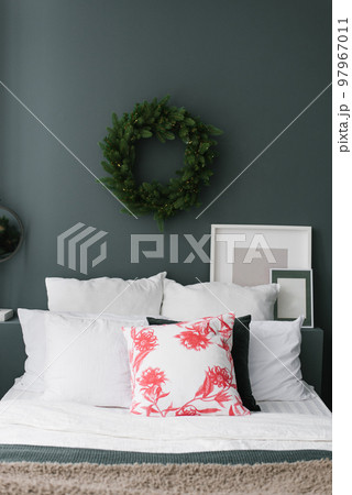 Pillows on the bed with a christmas wreath hanging over it on a dark wall 97967011