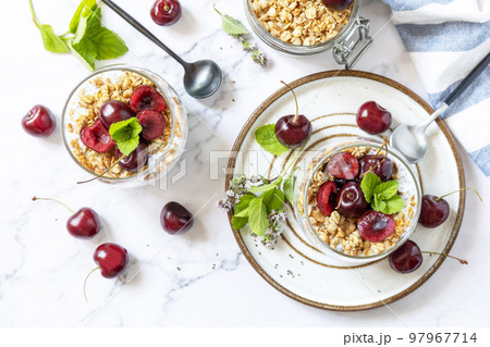 Healthy menu concept. Home made granola breakfast. Glass of parfait made of granola, berries cherry, yogurt with chia seeds on rustic table. View from above. 97967714