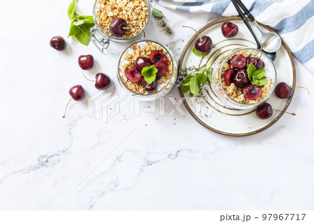 Healthy menu concept. Home made granola breakfast. Glass of parfait made of granola, berries cherry, yogurt with chia seeds on rustic table. View from above. Copy space. 97967717
