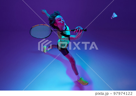 Top view. Portrait of teen boy in uniform playing badminton, returning shuttlecock in a run over blue purple background in neon ligth 97974122