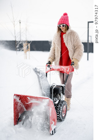 Woman removes snow from pathway with a snow thrower machine Woman removes snow from pathway with a snow thrower machine 97974317
