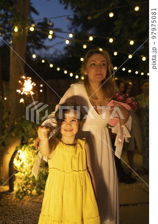 Mother bride with little cute daughter holding burning Bengal lights outdoors at wedding party Mother bride with little cute daughter holding burning Bengal lights outdoors at wedding party 97975081