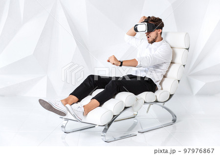 Excited young man is getting experience using VR-headset glasses of virtual reality gesticulating with his hands Excited young man is getting experience using VR-headset glasses of virtual reality gesticulating with his hands 97976867
