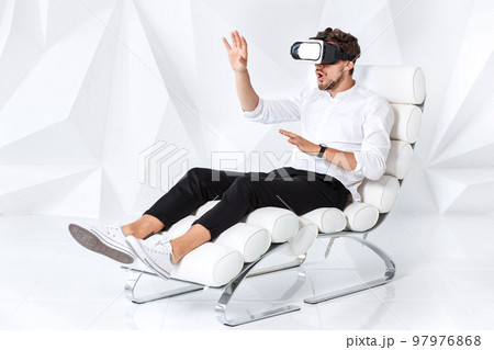 Excited young man is getting experience using VR-headset glasses of virtual reality gesticulating with his hands Excited young man is getting experience using VR-headset glasses of virtual reality gesticulating with his hands 97976868