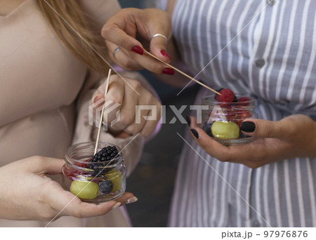 Glasses jar with a salad of fruits and berries in the hands of a female friends 97976876