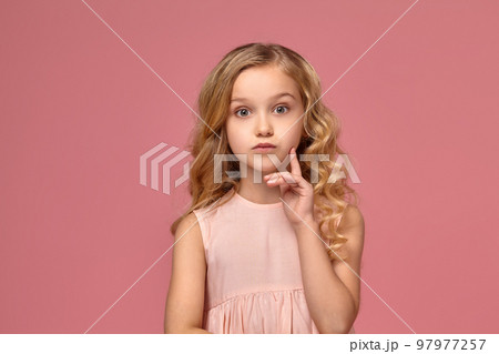 Little girl with a blond curly hair, in a pink dress is posing for the camera 97977257