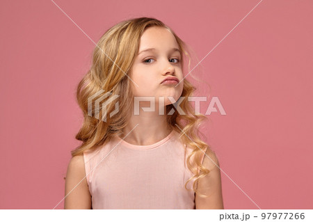 Little girl with a blond curly hair, in a pink dress is posing for the camera Little girl with a blond curly hair, in a pink dress is posing for the camera 97977266