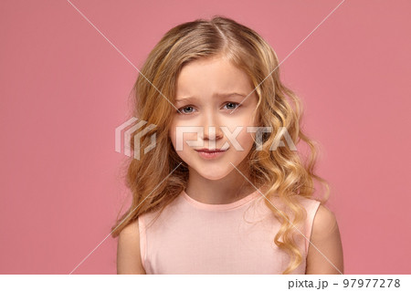 Little girl with a blond curly hair, in a pink dress is posing for the camera Little girl with a blond curly hair, in a pink dress is posing for the camera 97977278