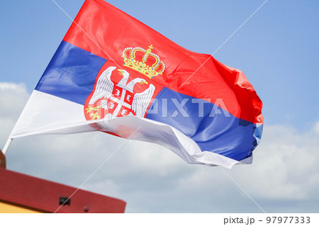 The flag of serbia against the blue sky flutters in the wind. Flag of a country in Europe. The flag of serbia against the blue sky flutters in the wind. Flag of a country in Europe. 97977333