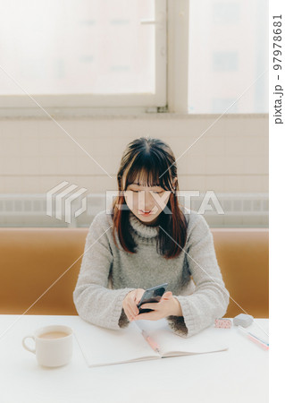 カフェで勉強中にスマホを触る若い女子大生の写真 97978681