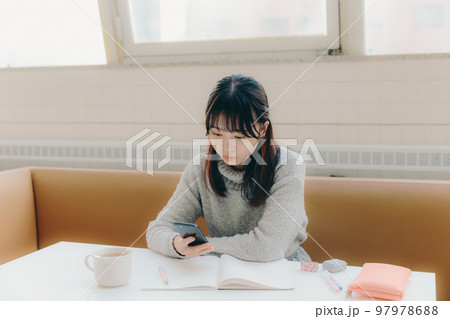 カフェで勉強中にスマホを触る若い女子大生の写真 97978688