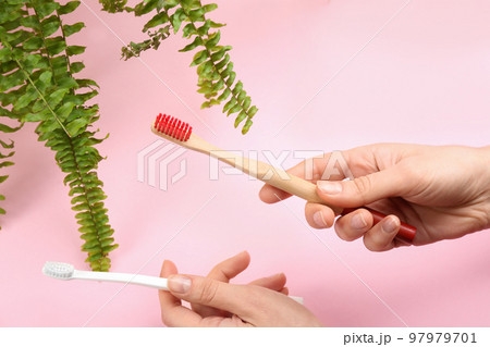 Woman holding natural bamboo and plastic toothbrushes on pink background 97979701