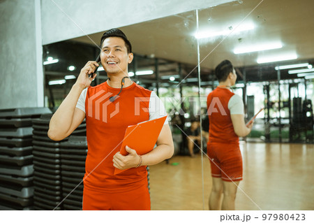 male instructor standing near mirror making phone call after workout 97980423