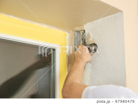 Man plastering window area with putty knife indoors, closeup. Interior repair Man plastering window area with putty knife indoors, closeup. Interior repair 97980479