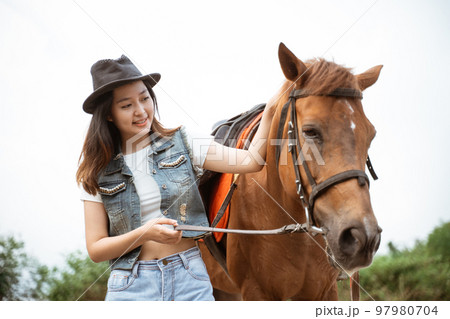beautiful asian cowboy girl standing beside horse on outdoor background 97980704