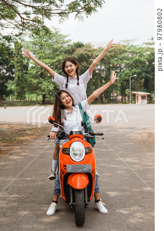 Two high school girls riding motorbikes standing while celebrating graduation 97980802