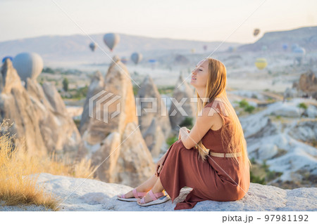 Tourist woman looking at hot air balloons in Cappadocia, Turkey. Happy Travel in Turkey concept. Woman on a mountain top enjoying wonderful view 97981192