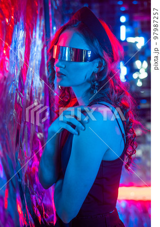 Close-up portrait of caucasian woman in sunglasses in neon light against foil wall. Close-up portrait of caucasian woman in sunglasses in neon light against foil wall. 97987257