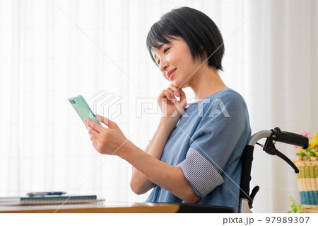 車椅子に座りながらスマートフォンを操作する若い女性 多様性社会イメージ 車椅子に座りながらスマートフォンを操作する若い女性 多様性社会イメージ 97989307