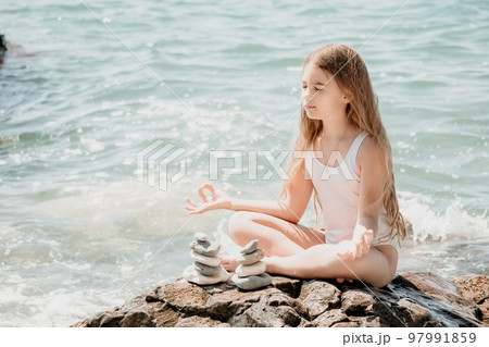 Woman with daughter bilds stones pyramid on seashore on a sunny day on the blue sea background. Happy family holidays. Pebble beach, calm sea. Concept of happy vacation on the sea, meditation, spa 97991859