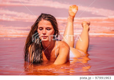 Young woman with long hair in pink salty lake with crystals of salt. Extremely salty pink lake, colored by microalgae with crystalline salt depositions. Spa, beauty and health care concept. 97991963