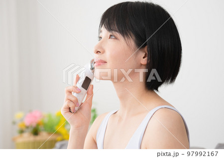 部屋で美顔器を使っている若い女性　美容イメージ	 97992167