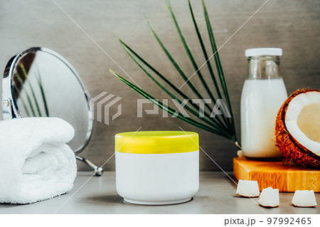 Beauty spa skincare cosmetic mockup cream package with coconut oil, fresh coconut, towel and mirror on dark gray background. Natural spa cosmetics concept. Selective focus, copy space. Beauty spa skincare cosmetic mockup cream package with coconut oil, fresh coconut, towel and mirror on dark gray background. Natural spa cosmetics concept. Selective focus, copy space. 97992465