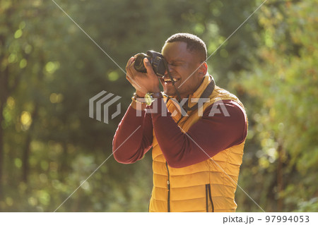 Close-up african american guy photographer taking picture with photo camera on city green park - leisure activity, diversity and hobby concept 97994053