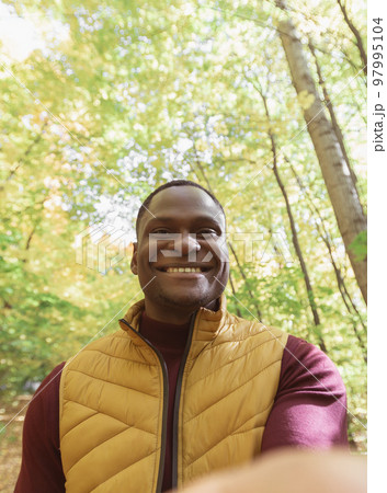 African American man taking a self portrait with a smartphone in autumn fall or video call portrait. Happy people, season and videocall concept African American man taking a self portrait with a smartphone in autumn fall or video call portrait. Happy people, season and videocall concept 97995104