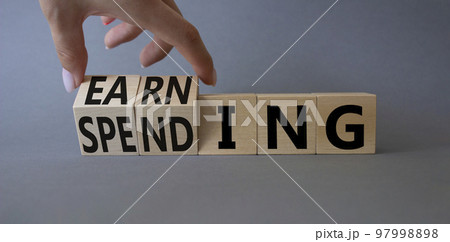 Earning and Spending symbol. Businessman hand. Turned cubes with words Earning and Spending. Beautiful grey background. Business and Earning and Spending concept. Copy space 97998898