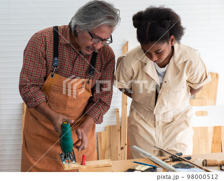 Teenaged girls learn to use an electronic saw and play with their grandfather in the wooden workshop, a concept for enhancing the development and thinking of children. 98000512