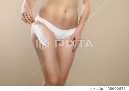 Woman with feather showing smooth skin on beige background, closeup. Brazilian bikini epilation Woman with feather showing smooth skin on beige background, closeup. Brazilian bikini epilation 98000821
