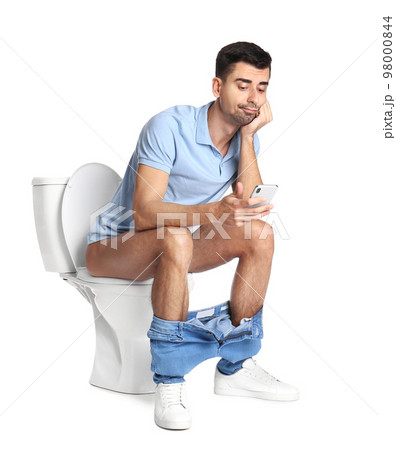 Emotional man with smartphone sitting on toilet bowl, white background Emotional man with smartphone sitting on toilet bowl, white background 98000844