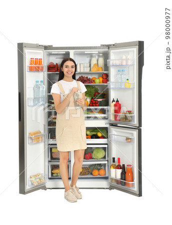 Young woman with bottle of water near open refrigerator on white background Young woman with bottle of water near open refrigerator on white background 98000977