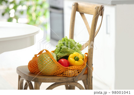 Net bag with vegetables on wooden chair in kitchen Net bag with vegetables on wooden chair in kitchen 98001041