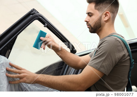 Worker washing tinted car window in workshop 98001077