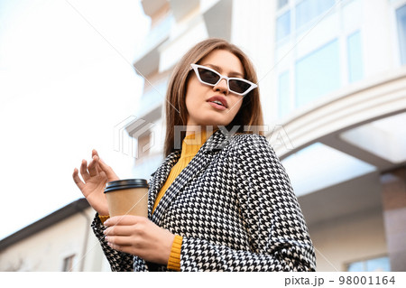 Young woman with cup of coffee on city street in morning 98001164